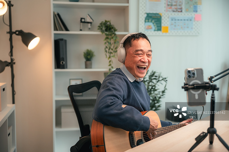 快乐的老年人一边弹吉他一边在智能手机上直播图片素材