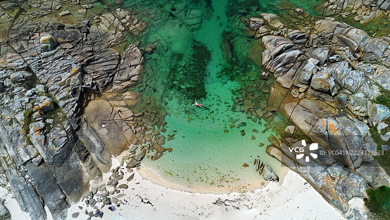 航拍照片，单身男子在西班牙加利西亚蓬特韦德拉的卡雷龙自然公园内，阿罗萨岛南部美丽的海湾中享受阳光和海滩的一天。图片素材