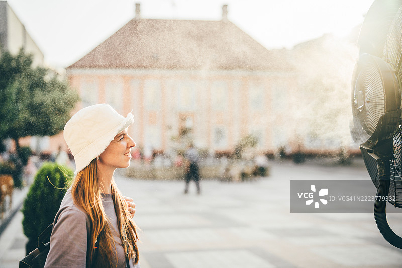 一位女性在炎热的夏日里，在美丽的欧洲城市中走动时，站在风扇前降温。图片素材