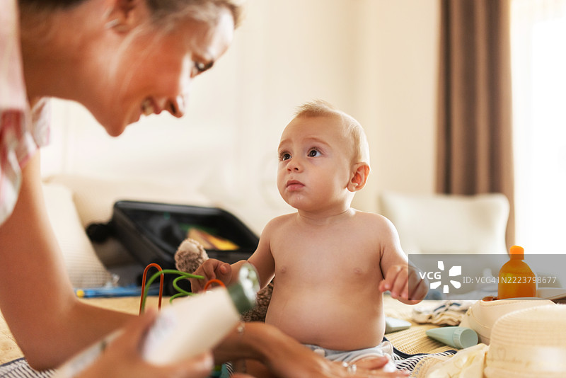 关心的母亲在床上给她的宝宝涂抹防晒霜，为户外阳光明媚的一天做准备图片素材
