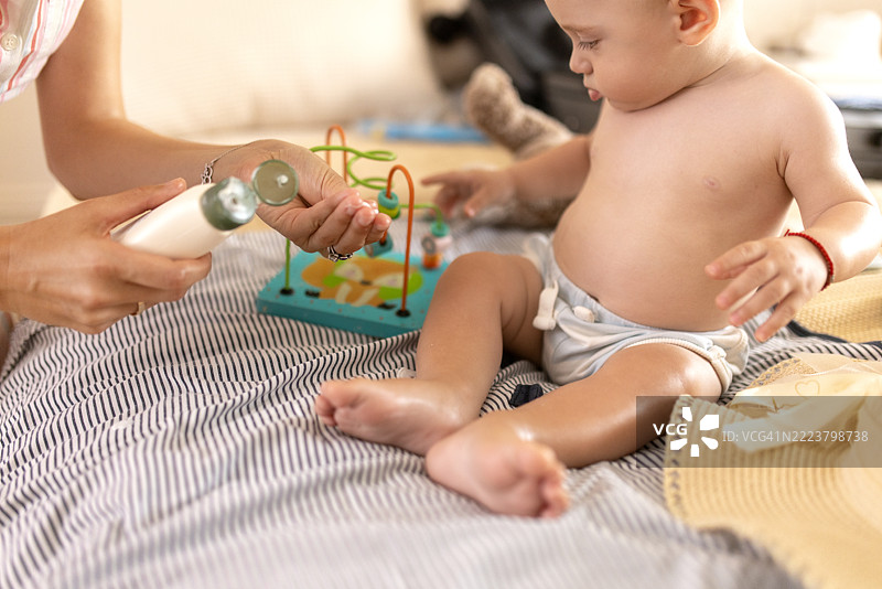 关心的母亲在床上给她的宝宝涂抹防晒霜，为户外阳光明媚的一天做准备图片素材