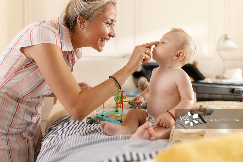 关心的母亲在床上给她的宝宝涂抹防晒霜，为户外阳光明媚的一天做准备图片素材