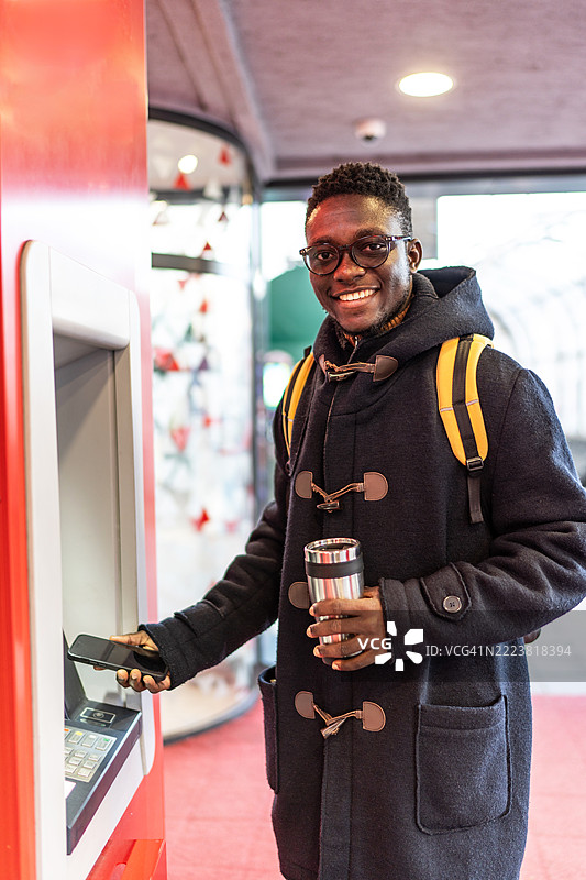 年轻男子使用智能手机在自动取款机取款图片素材