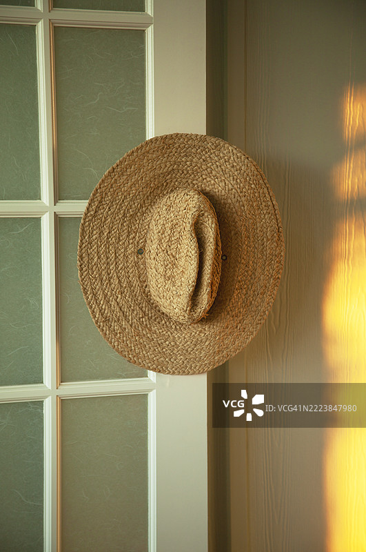 从打开的法式门上挂着的草编太阳帽。图片素材