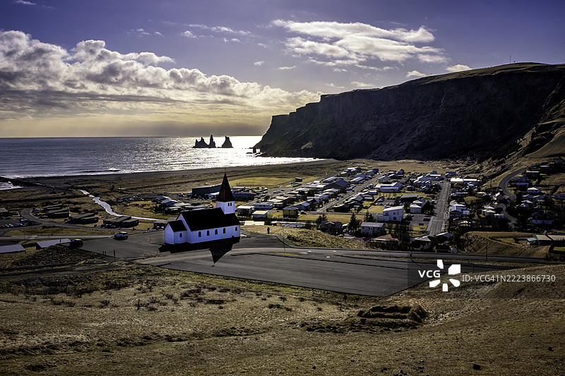 一个村庄位于雷尼斯德兰加尔玄武岩海堆和雷尼斯山悬崖前面图片素材