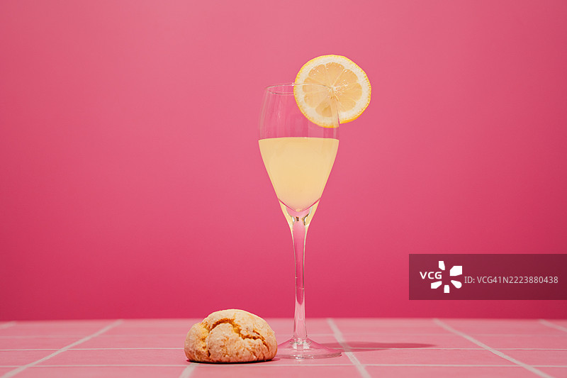 粉色桌子和粉色背景上的柠檬酒饮料杯，旁边有柠檬饼干，留有空白空间。图片素材