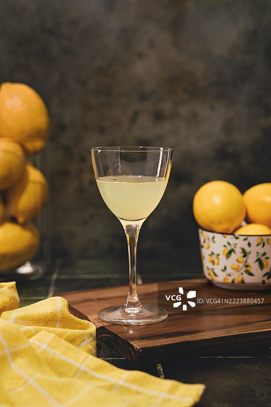柠檬酒饮品，桌上放着一个酒杯，配有黄色格子餐巾和柠檬，留白空间。地中海花园氛围图片素材