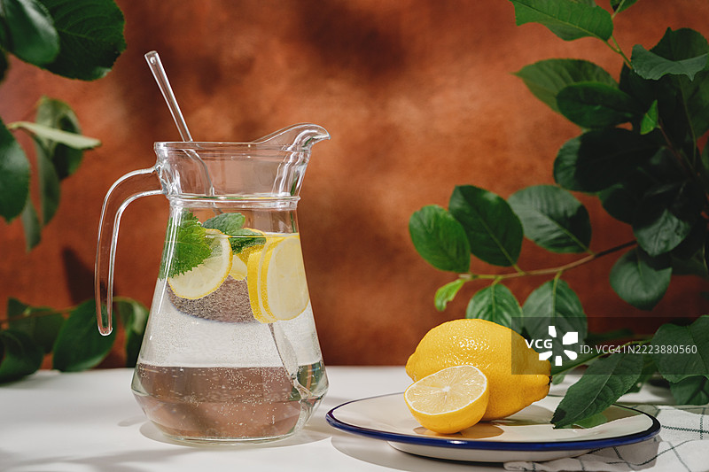 花园桌上放着柠檬水壶和几个新鲜的柠檬。夏日氛围。陶土墙。图片素材