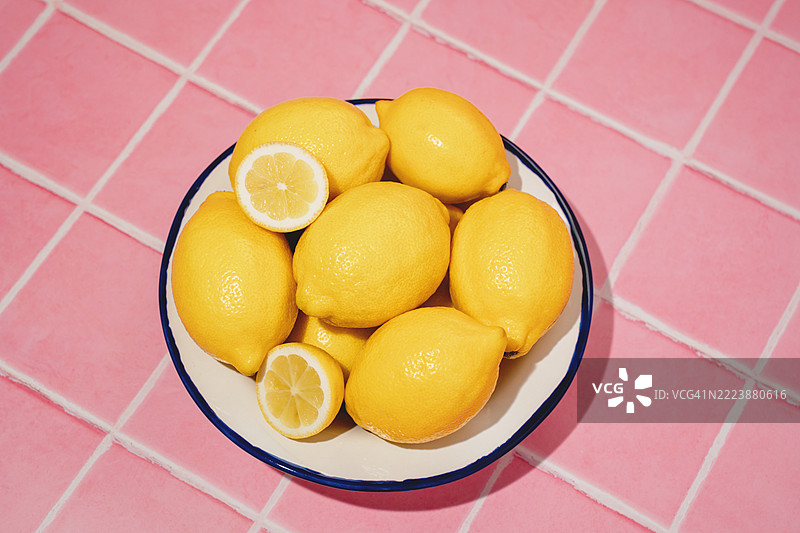 几个完整和切开的新鲜柠檬放在粉色桌子上的碗里。夏季花园。俯视图图片素材