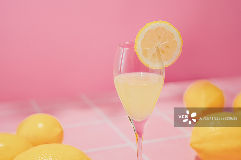 柠檬酒饮料。几颗新鲜的完整柠檬散落在粉色桌子上，粉色背景留有空白空间。夏季花园。图片素材