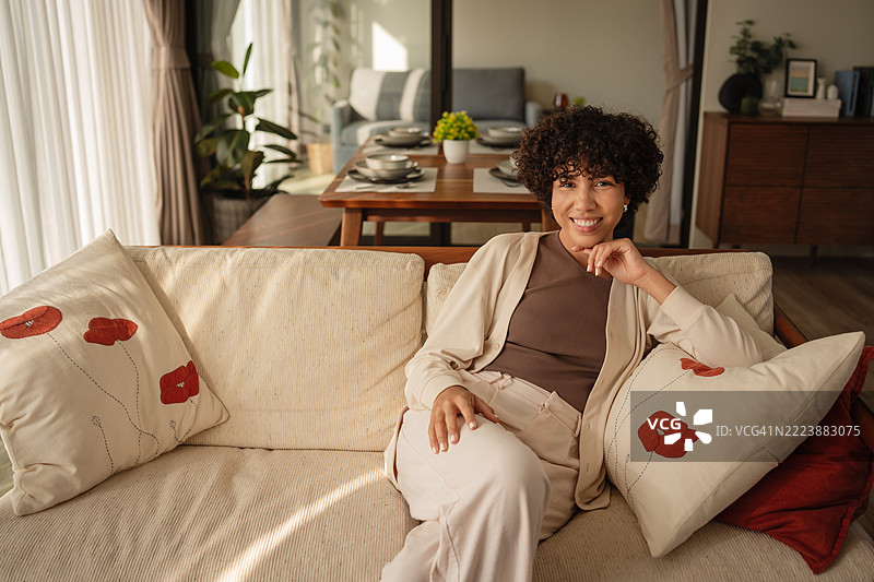 年轻女性在家中舒适的沙发上放松，微笑着看向镜头图片素材