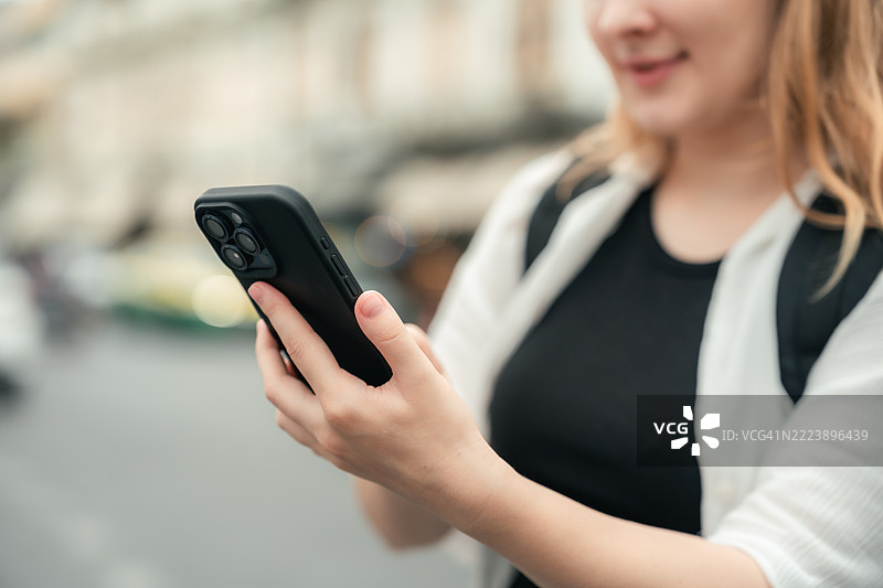 女性游客使用智能手机查看地图，在繁忙的城市街道中导航。图片素材