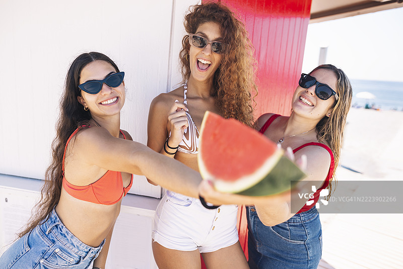 三位女性在海滩上展示一块西瓜图片素材