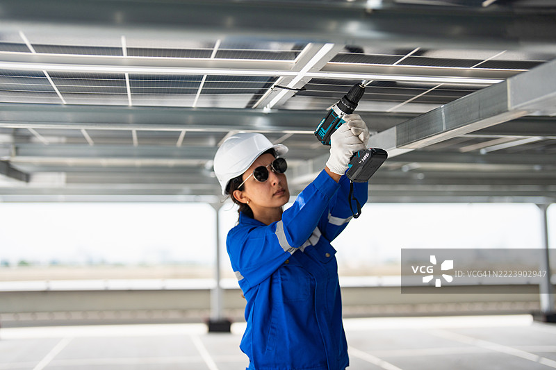 一名女性太阳能面板工人正在使用电钻安装屋顶上的太阳能面板。图片素材