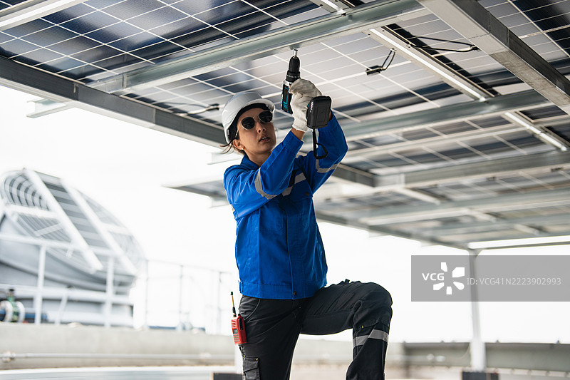 一名女性太阳能面板工人在屋顶上使用电钻安装太阳能面板。图片素材