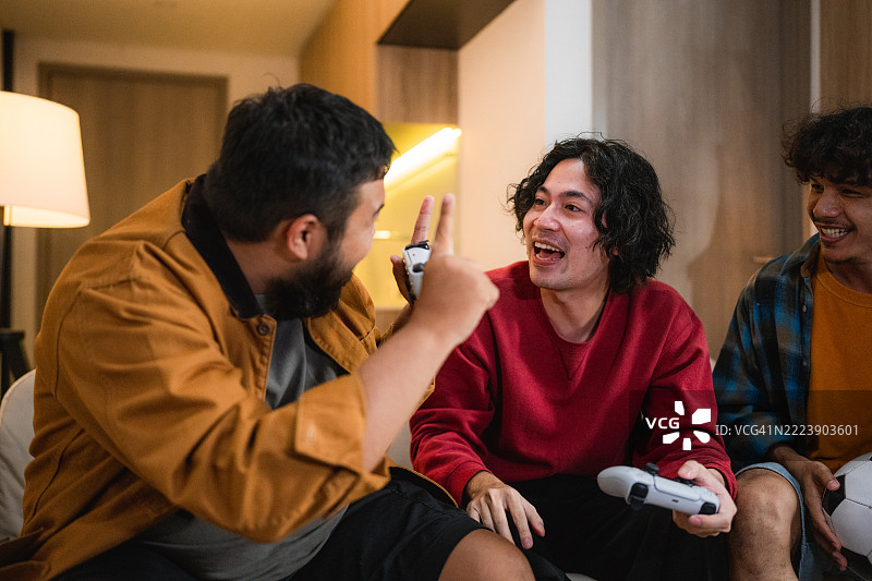 一群朋友沉浸在足球视频游戏中，每个人都专注而兴奋地握着游戏手柄，互相竞争并在比赛的激烈氛围中欢呼。图片素材
