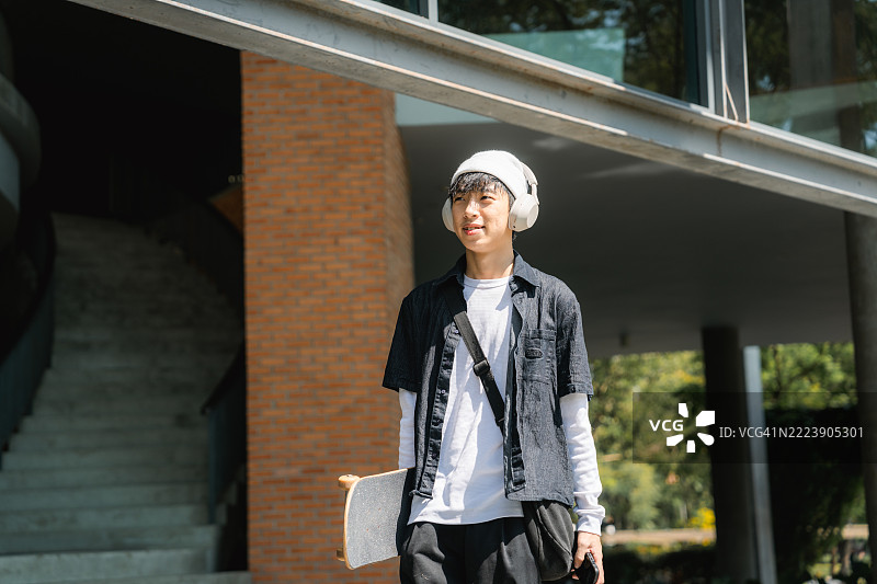 微笑的大学生在校园里走着，手持数字平板，戴着耳机听音乐图片素材