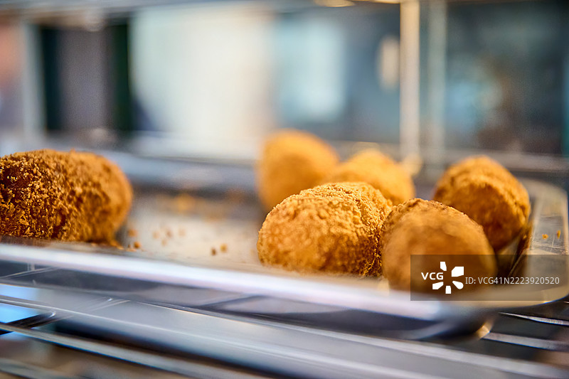 金棕色的面包裹苏格兰蛋静静地放在一个反光金属容器中，温暖的灯光照耀着它们。图片素材