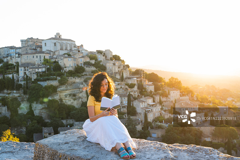 在法国普罗旺斯-阿尔卑斯-蓝色海岸的戈尔德斯，女人在日出时分户外阅读一本书。图片素材