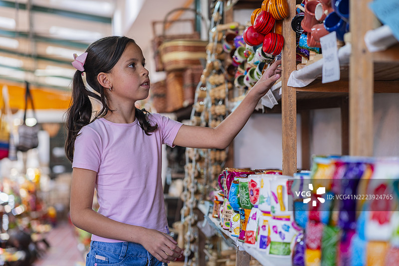 一位来自哥伦比亚波哥大的拉丁裔女孩，年龄在10到14岁之间，在博亚卡省拉基拉镇的一家手工艺品店购物。图片素材