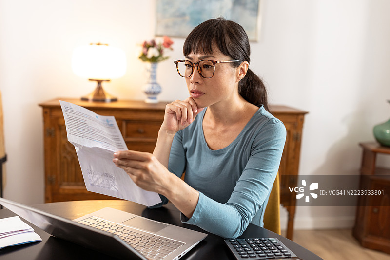 一位女性在家办公桌前使用笔记本电脑审阅文件图片素材