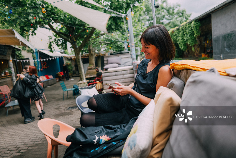 在户外城市咖啡馆放松的女性，手持智能手机并微笑图片素材