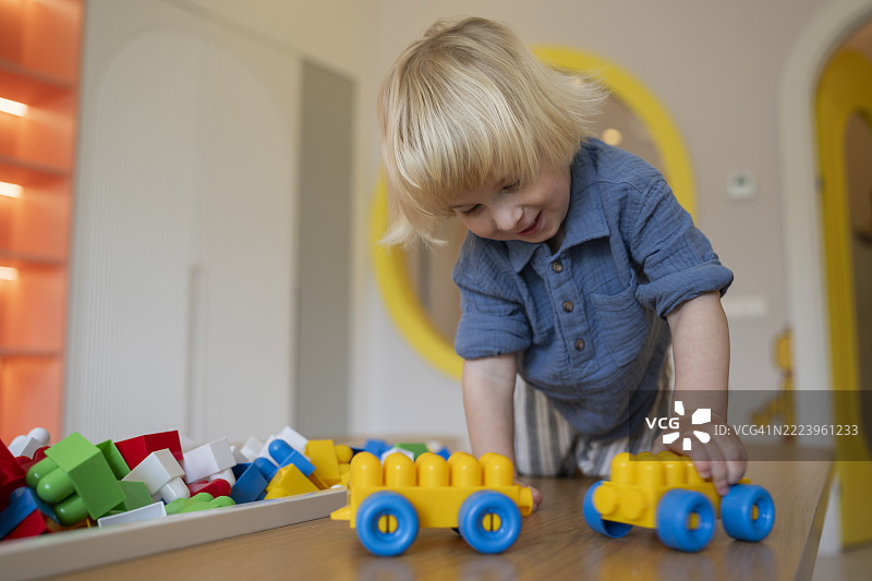 快乐的小金发男孩在玩积木，笑得很开心。图片素材
