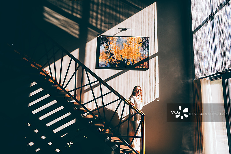 一位孤独的女性站在楼梯上，身处戏剧性的光影室内。图片素材
