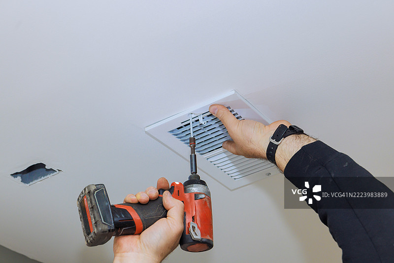 房主在天花板上使用电钻修理暖通空调通风口图片素材