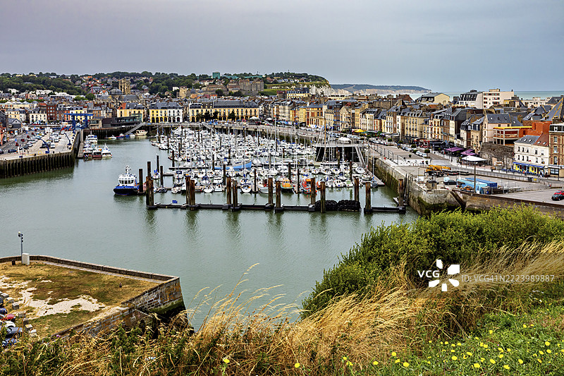 法国诺曼底的迪耶普港口小镇，前景有许多船只和绿色植物，天空多云。图片素材