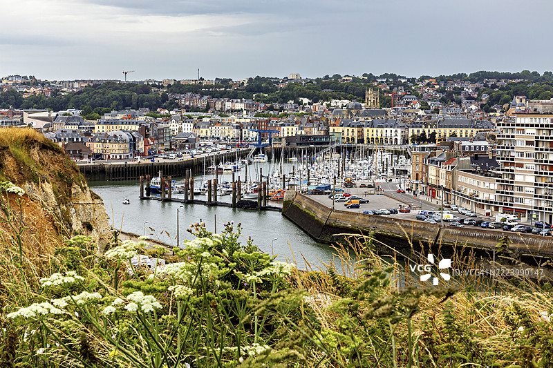 诺曼底的迪耶普港口，停泊着船只，五彩斑斓的建筑和绿色植物在阴 cloudy 的天空下。图片素材