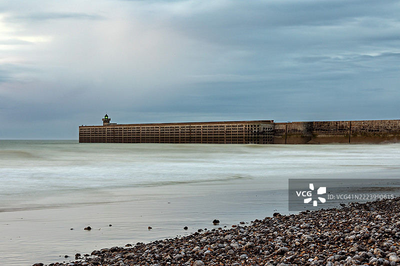 一座防波堤伸入海中，周围是卵石海滩和多云的天空，法国诺曼底的迪耶普码头和海滩。图片素材