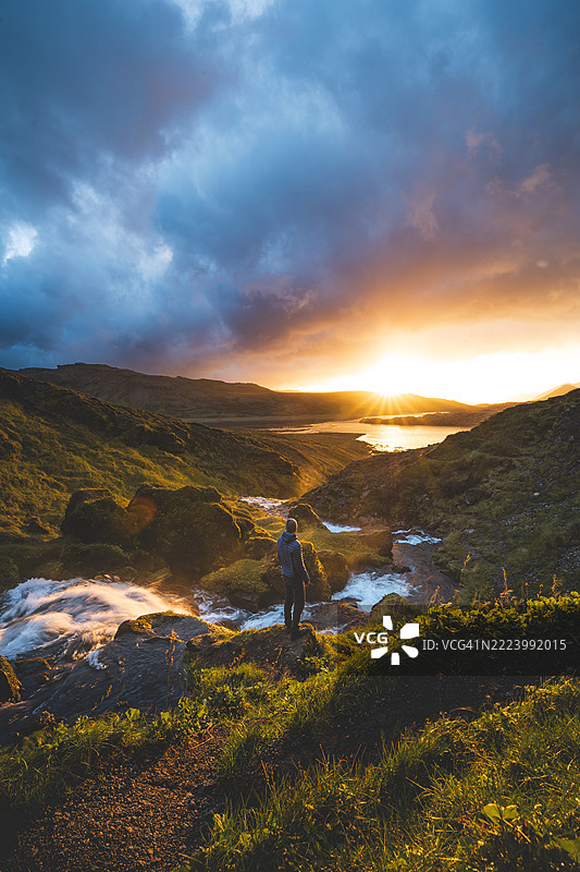 男子在冰岛西部斯奈法尔斯半岛的塞尔瓦拉瀑布下欣赏神奇的日落景色，站在清澈的冷水下，感受大自然的珍宝，维斯图兰，冰岛。图片素材