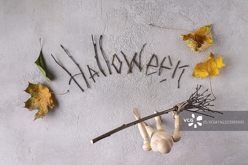 一个木制人用扫帚扫走由树枝和秋叶组成的“万圣节”字样，俯视图图片素材
