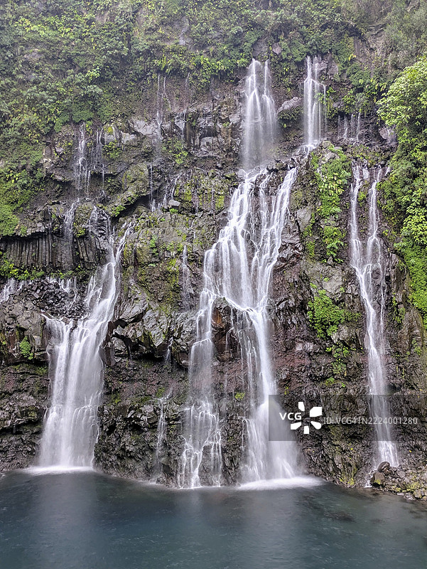 水流从岩石悬崖上倾泻而下，四周环绕着郁郁葱葱的绿植，形成宁静的自然景观，留尼旺岛，法国，非洲图片素材