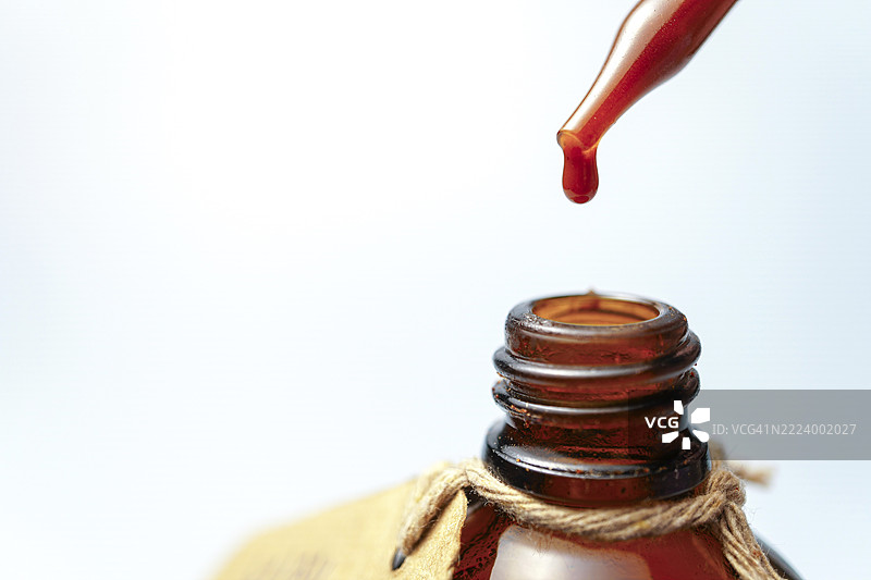 红色液体从移液管滴入琥珀色瓶子，与浅色背景形成视觉上吸引人的对比图片素材