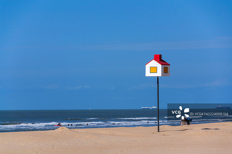 沙滩上竖着一根杆子的红屋顶木制房屋模型，位于比利时西弗拉芒省的德汉沿海村庄。图片素材