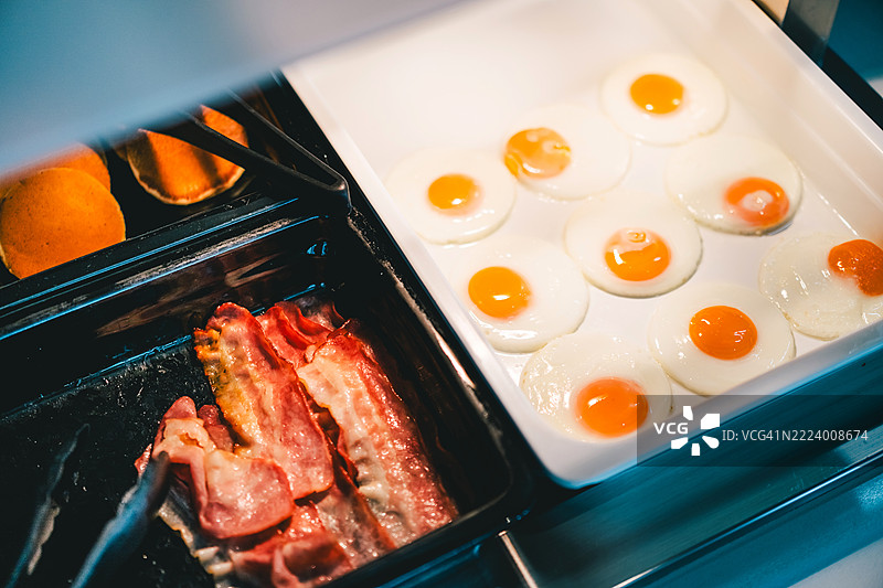 在温暖的灯光下，托盘中展示的煎蛋和培根图片素材