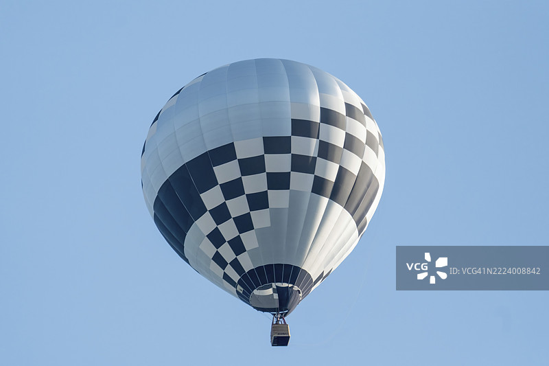 格子图案的热气球在晴朗的蓝天中漂浮，呈现出独特而迷人的景象图片素材