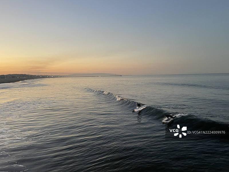 四个冲浪者在日出时的海浪上，橙色桃色的朦胧天空，加利福尼亚州马里布， 美国图片素材