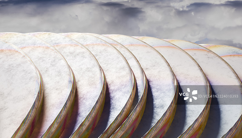 一堆彩虹色的圆盘在多云的天空下形成波浪形状图片素材