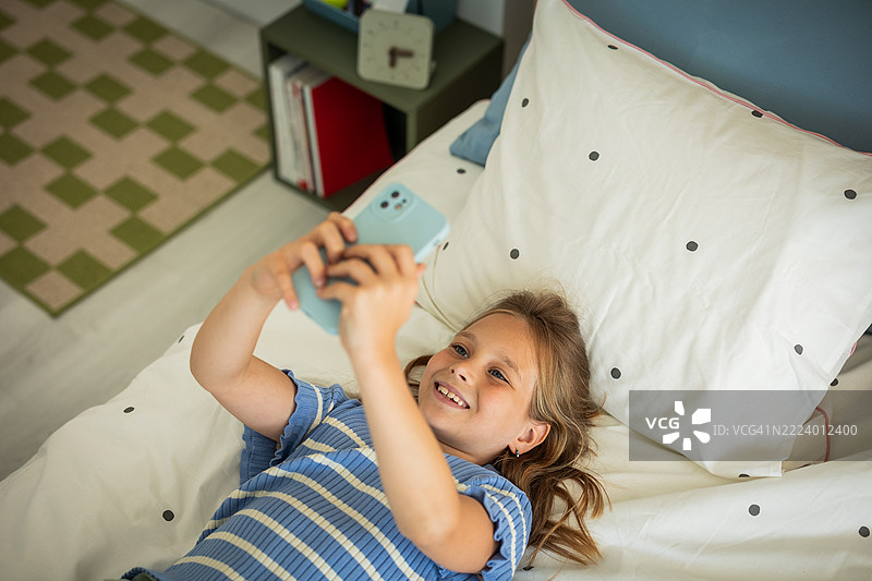 小女孩在卧室里躺在床上使用智能手机图片素材