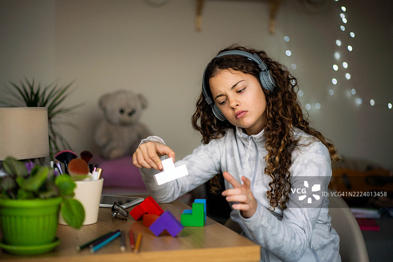 快乐的少女坐在房间的桌子旁，戴着耳机，边唱边跳，听着音乐，桌上放着一本书。图片素材