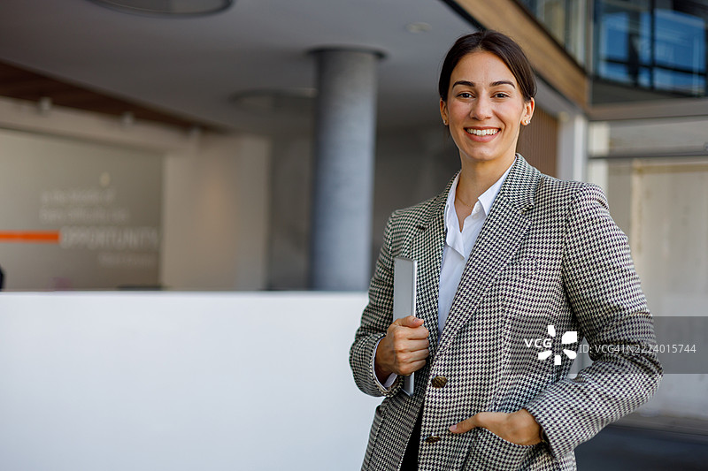 微笑的职业女性，手持数字平板，站在时尚的企业大堂中图片素材