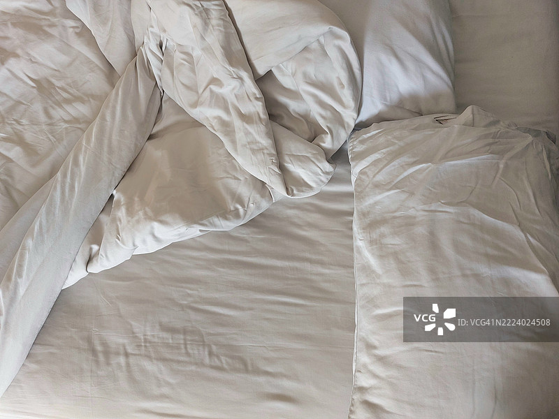 未整理的白色床铺，晨光中皱褶的床单图片素材