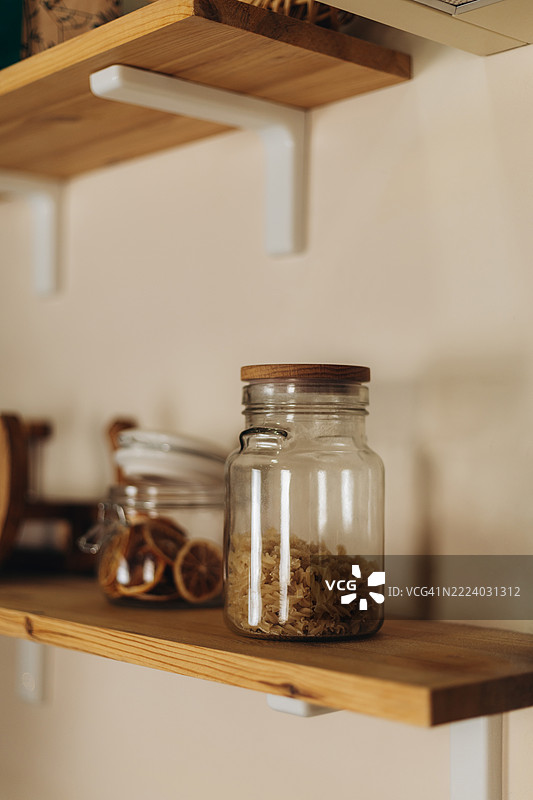 木制架子上摆放着装满干意大利面的玻璃罐和干燥的柑橘片。图片素材