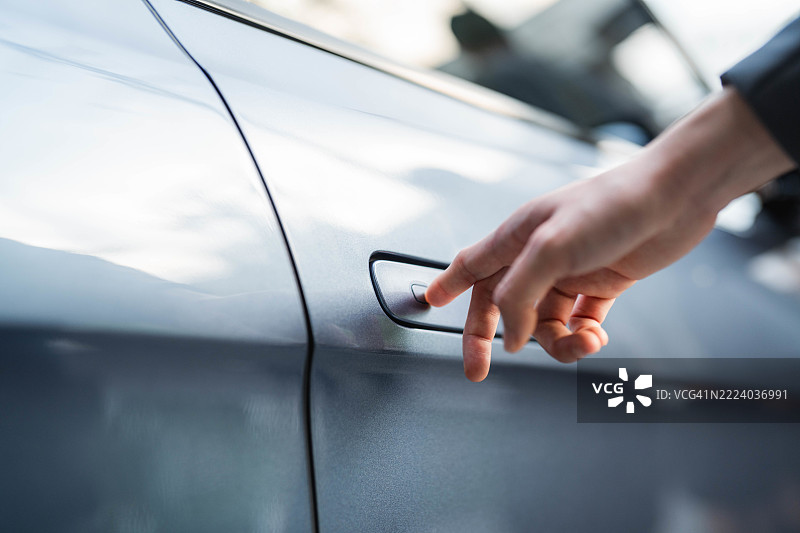一位女性按下电动车车门把手上的按钮解锁车门图片素材