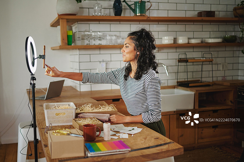 创意年轻女性在家中使用环形灯和智能手机为她的在线可持续业务按下录制按钮。图片素材