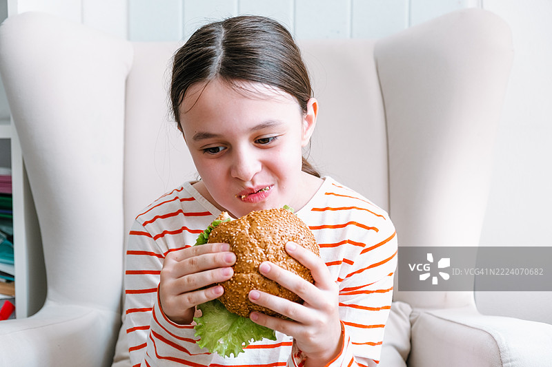 9岁女孩坐在椅子上吃自制汉堡。图片素材