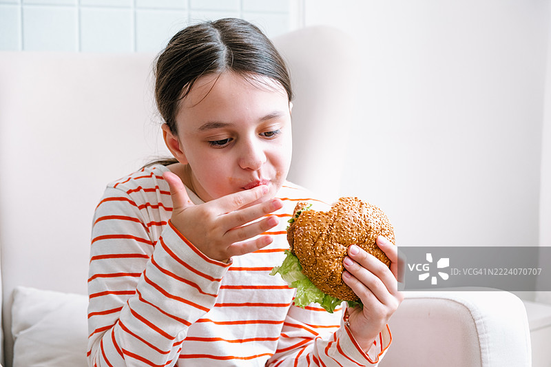 9岁女孩坐在椅子上吃自制汉堡。图片素材